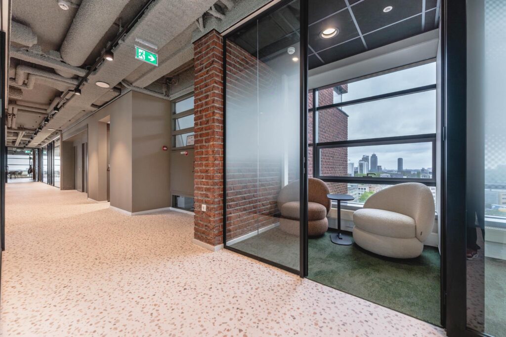 Modern office hallway at Joop Geesinkweg with a glass-walled seating area overlooking the city skyline.